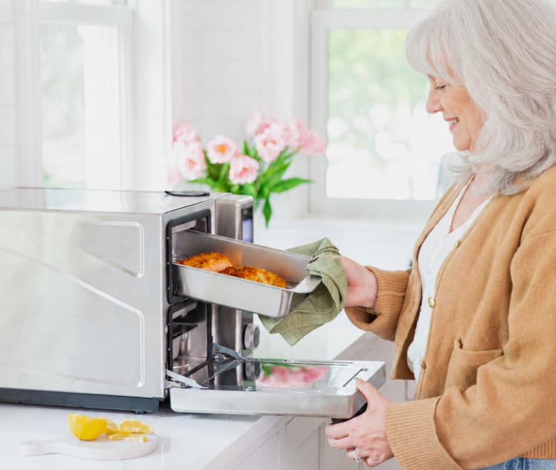 Woman removing a cooked meal tray from a Suvie in a bright kitchen