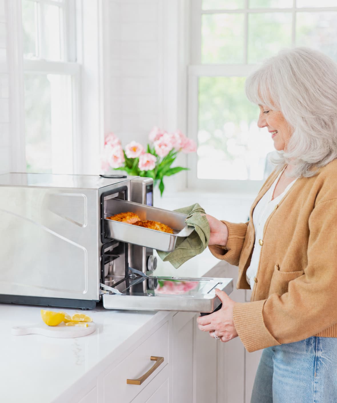 Woman removing a cooked meal tray from a Suvie in a bright kitchen
